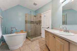 Bathroom with a stall shower, lofted ceiling, tile patterned flooring, vanity, and a freestanding tub