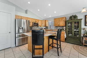 Kitchen featuring a center island, light tile patterned floors, stainless steel appliances, light countertops, and vaulted ceiling