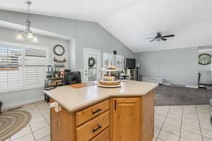 Kitchen with light tile patterned floors, ceiling fan with notable chandelier, visible vents, vaulted ceiling, and light countertops