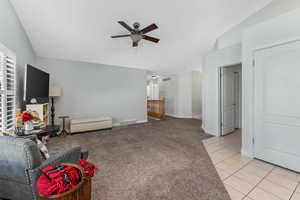 Living room featuring light tile patterned floors, light colored carpet, visible vents, ceiling fan, and vaulted ceiling