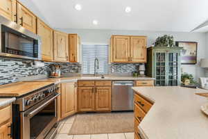 Kitchen featuring lofted ceiling, light countertops, appliances with stainless steel finishes, light tile patterned flooring, and a sink