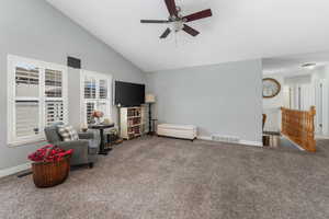 Living area with lofted ceiling, carpet flooring, and an upstairs landing