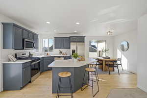 Kitchen with light wood finished floors, a kitchen bar, appliances with stainless steel finishes, and light countertops