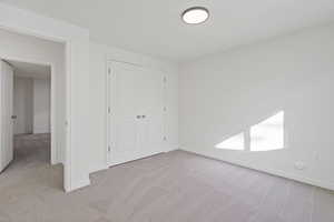 Unfurnished bedroom featuring baseboards, a closet, and light colored carpet