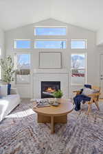 Living room featuring carpet floors, a fireplace, high vaulted ceiling, and baseboards