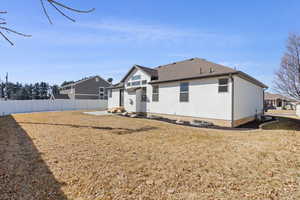 Rear view of house featuring roof with shingles, fence, a lawn, and stucco siding