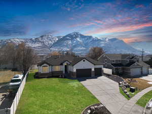 View of front facade with driveway, an attached garage, fence, a mountain view, and a front yard