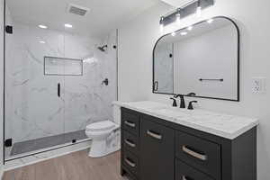 Full bathroom with a marble finish shower, visible vents, toilet, vanity, and wood finished floors