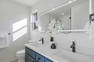 Bathroom featuring toilet, double vanity, a marble finish shower, and a sink