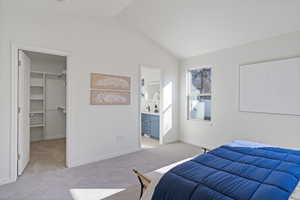 Bedroom featuring a walk in closet, light colored carpet, vaulted ceiling, ensuite bath, and baseboards