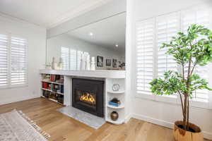 Interior space with a fireplace with flush hearth, baseboards, crown molding, and wood finished floors