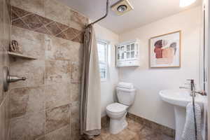 Bathroom with toilet, baseboards, and a tile shower