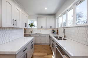 Kitchen featuring a sink, light wood-style floors, dishwasher, and light stone countertops