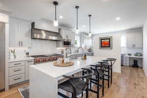 Kitchen featuring stainless steel appliances, a sink, wall chimney range hood, light wood-type flooring, and a kitchen breakfast bar