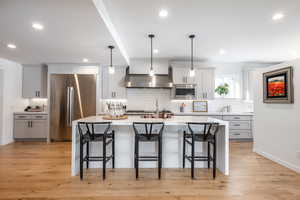 Kitchen with stainless steel appliances, wall chimney exhaust hood, a breakfast bar area, and light countertops