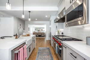 Kitchen featuring light wood-style flooring, hanging light fixtures, appliances with stainless steel finishes, wall chimney exhaust hood, and tasteful backsplash