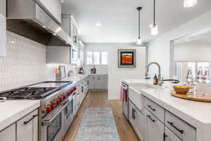 Kitchen with light wood finished floors, tasteful backsplash, stainless steel appliances, wall chimney range hood, and a sink