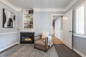 Sitting room with a lit fireplace, ornamental molding, built in features, and baseboards