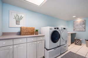 Clothes washing area with washing machine and clothes dryer, light tile patterned floors, recessed lighting, cabinet space, and baseboards