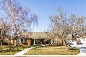 Ranch-style home featuring brick siding, a chimney, a front yard, a garage, and driveway