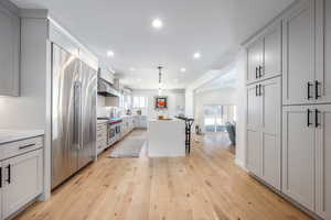 Kitchen featuring recessed lighting, a center island, wall chimney exhaust hood, light wood finished floors, and high end appliances