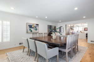 Dining area with light wood-style floors, crown molding, visible vents, and a wealth of natural light