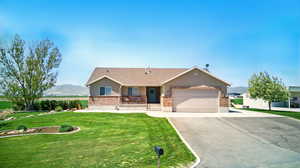 Single story home with driveway, brick siding, a mountain view, a garage, and a front lawn