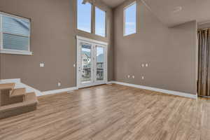 Unfurnished living room featuring light wood-style flooring, visible vents, a towering ceiling, stairs, and baseboards