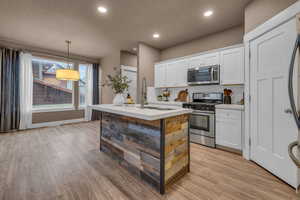 Kitchen with light wood finished floors, stainless steel appliances, recessed lighting, light countertops, and white cabinetry