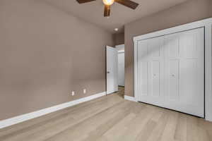 Unfurnished bedroom featuring light wood-style flooring, baseboards, ceiling fan, and a closet