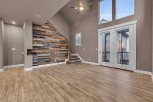 Unfurnished living room featuring wooden walls, an accent wall, wood finished floors, a ceiling fan, and stairs