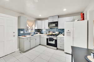 Kitchen featuring stainless steel gas stove, white refrigerator with ice dispenser, marble finish floor, black microwave, and a sink