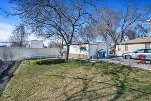 View of yard featuring driveway, a detached garage, a trampoline, fence, and an outdoor structure