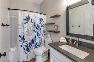 Bathroom with toilet, a shower with shower curtain, and vanity