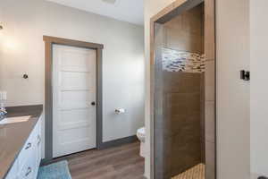 Bathroom with toilet, vanity, wood finished floors, tiled shower, and baseboards