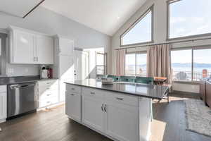 Kitchen featuring dark countertops, white cabinets, stainless steel dishwasher, and wood finished floors