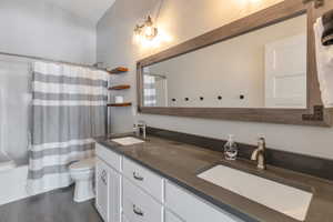 Full bathroom with toilet, double vanity, a sink, and wood finished floors