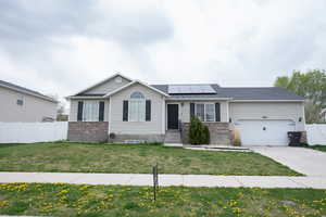 Ranch-style house with fence, solar panels, driveway, brick siding, and a front yard
