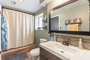 Bathroom featuring toilet, visible vents, vanity, decorative backsplash, and shower / bath combination with curtain