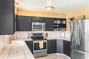 Kitchen featuring tile counters, a sink, stainless steel appliances, a textured ceiling, and backsplash