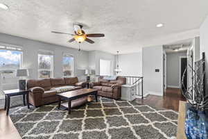 Living area with ceiling fan with notable chandelier, a textured ceiling, baseboards, and wood finished floors