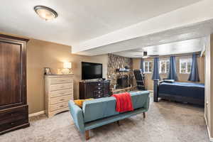 Bedroom with baseboards, a textured wall, a textured ceiling, a stone fireplace, and carpet floors