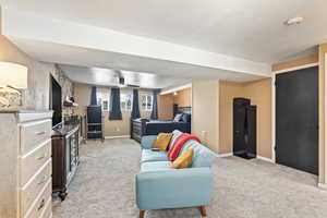 Living area with light carpet, a textured ceiling, a ceiling fan, and baseboards