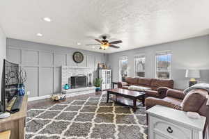 Living area featuring a ceiling fan, wood finished floors, a fireplace, a decorative wall, and recessed lighting