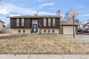 Bi-level home with an attached garage, fence, driveway, a chimney, and a front yard