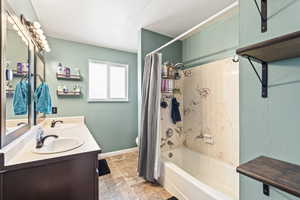 Full bath featuring double vanity, shower / tub combo, baseboards, and a sink