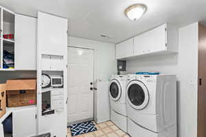 Washroom with cabinet space, visible vents, independent washer and dryer, a textured ceiling, and light floors