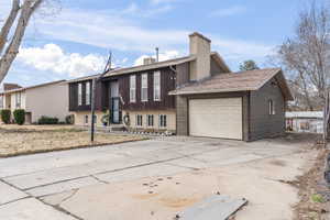 View of front of property featuring a garage, concrete driveway, and a chimney