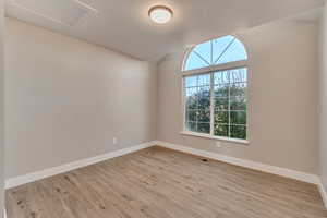 Unfurnished room featuring vaulted ceiling, light wood finished floors, visible vents, and baseboards