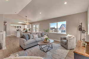 Living room featuring vaulted ceiling, light wood finished floors, a chandelier, and baseboards